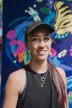 A person wearing a hat and jewelry in front of a brightly colored abstract image
