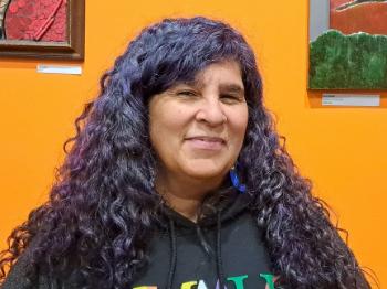 A person with long wavy black hair in front of an orange wall
