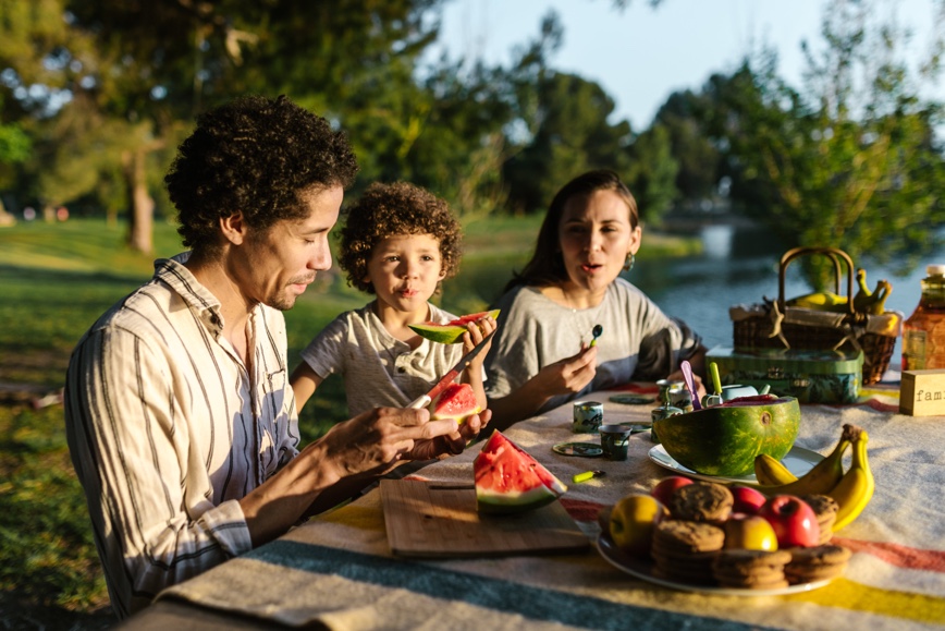 Family eating healthy food at picnic table in summer