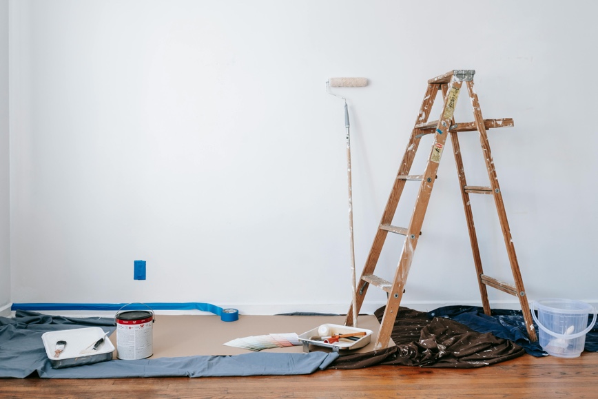 Ladder, tarps, paint, brushes in front of blank wall