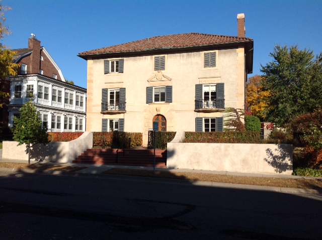 Color photo of house with tan exterior, red roof and green shutters taken from street in 2012.