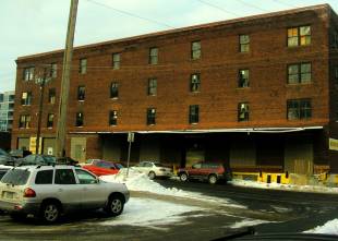 CoColor exterior photo of four-story red brick warehouse taken from parking lot in winter.