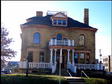 Color exterior photo of two story brick mansion with large front porch and balcony.