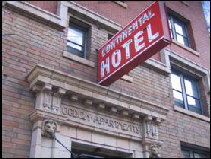 Color exterior photo of the red Continental Hotel sign with white letters attached to the exterior brick above the building entrance.