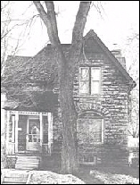 Sepia exterior image looking directly at the front of a two-story cottage-style limestone home.