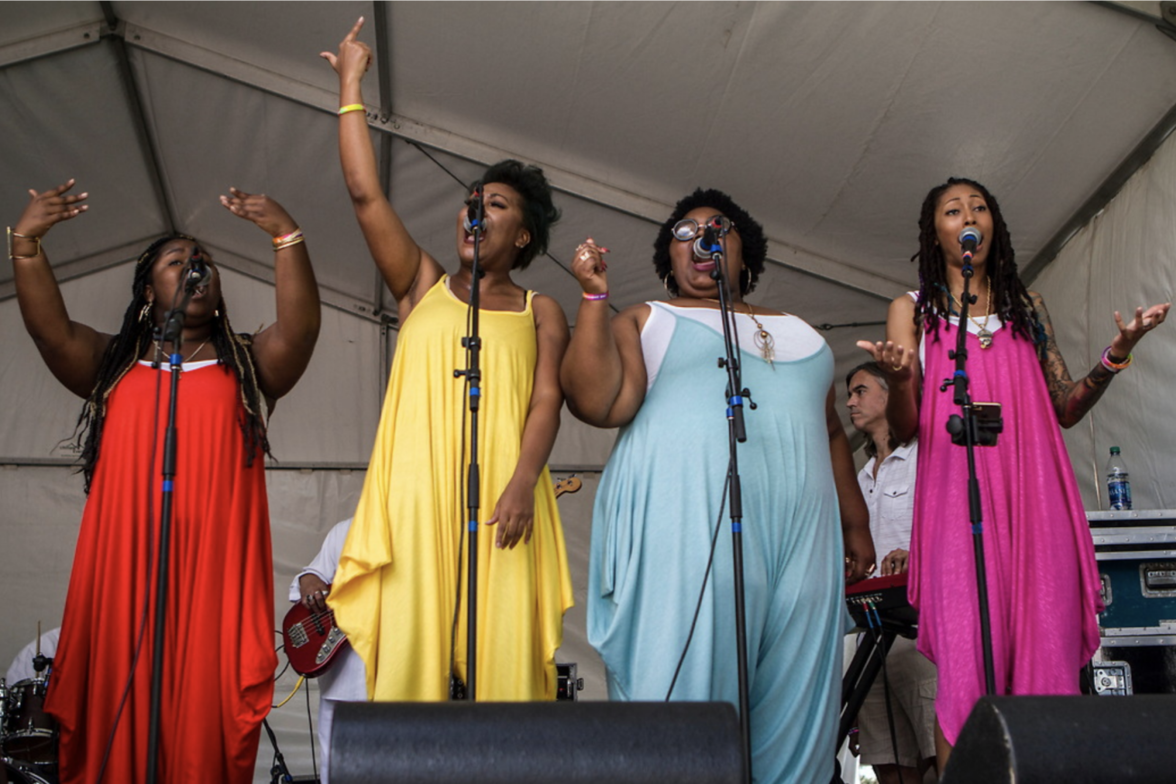 Four black women in colorful dresses singing live on stage